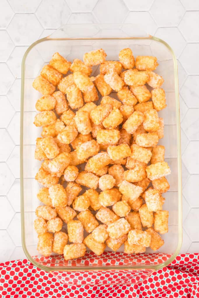 Frozen tater tots arranged in a glass 9x13-inch baking dish before baking.