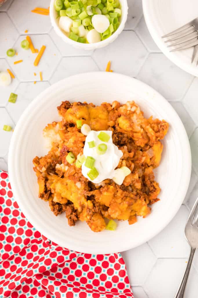 Overhead view of a plated serving of Chili Cheese Tater Tot Casserole topped with sour cream and sliced green onions.