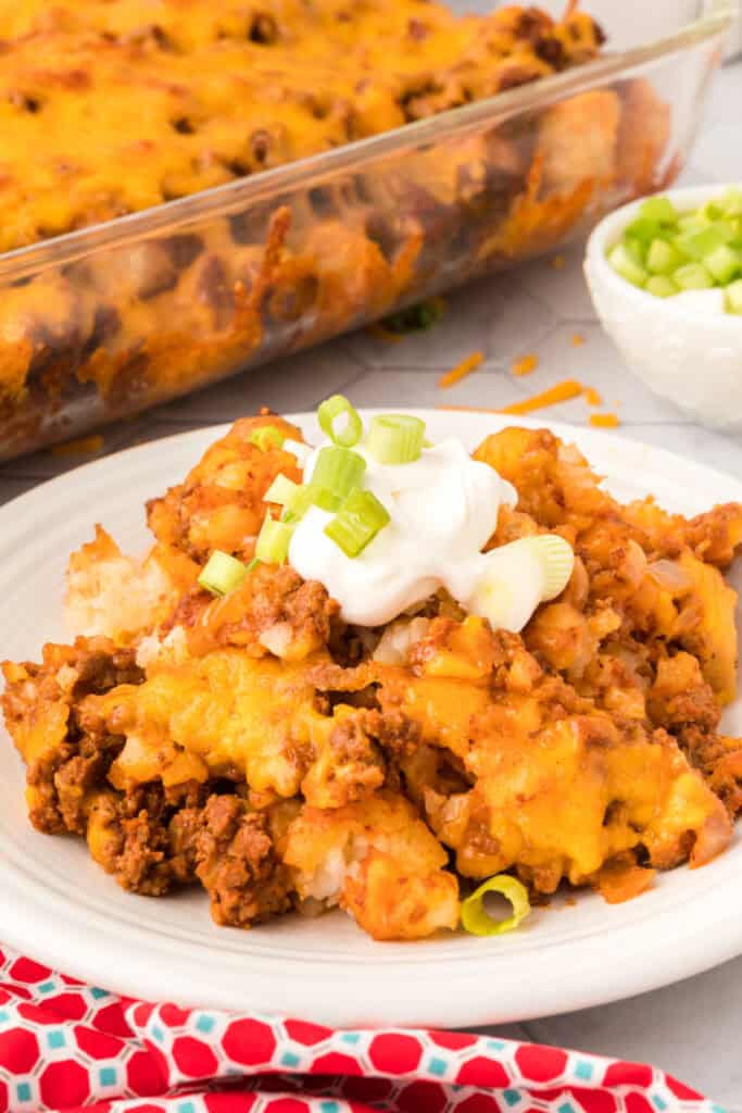 Close-up of Chili Cheese Tater Tot Casserole on a white plate topped with sour cream and sliced green onions.