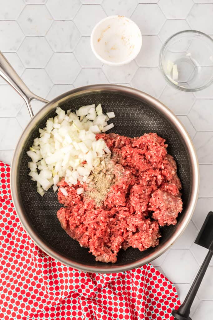 Raw ground beef, diced onion, salt, and pepper in a skillet before cooking for Chili Cheese Tater Tot Casserole.