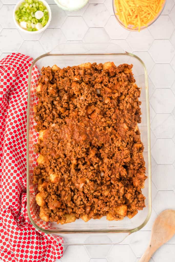 Layer of homemade chili spread over baked tater tots in a glass baking dish.
