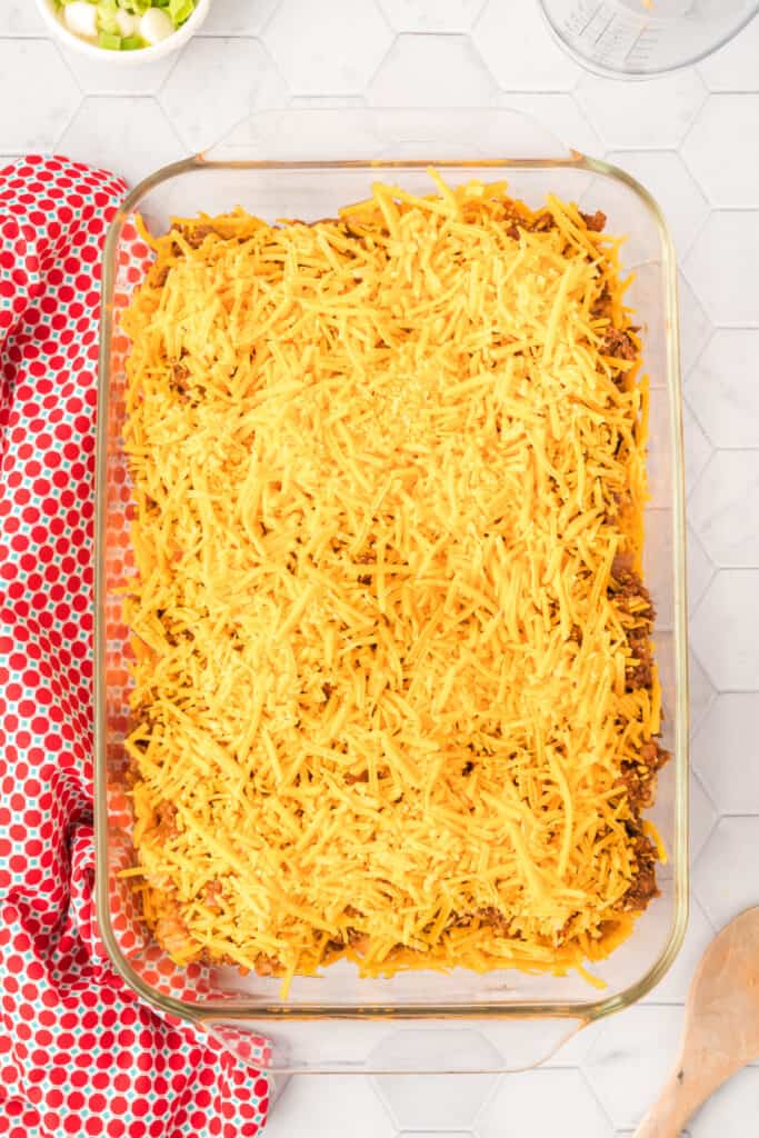 Shredded cheddar cheese covering the chili layer in a glass baking dish before baking.