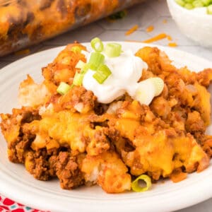 Square-cropped image of Chili Cheese Tater Tot Casserole topped with sour cream and sliced green onions on a white plate.