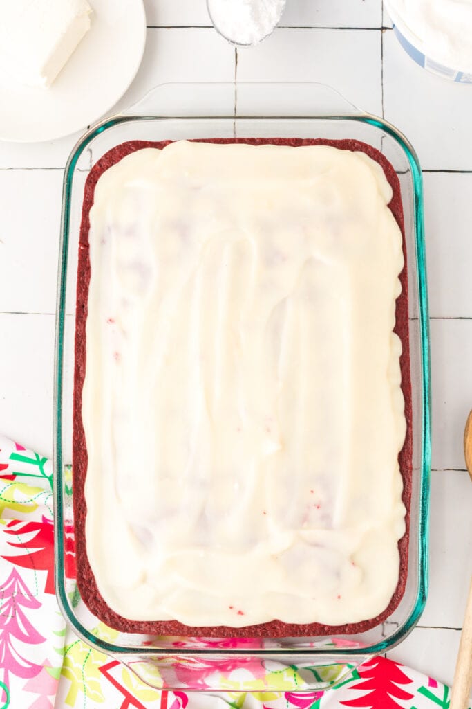 Red velvet cake in a glass baking dish topped with white chocolate pudding spread across the surface.