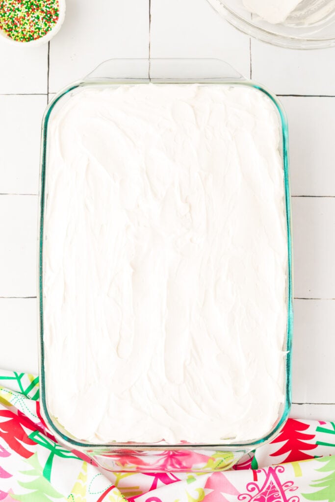 Red velvet poke cake in a 9x13-inch glass baking dish topped with a smooth layer of white cream cheese topping before adding sprinkles.