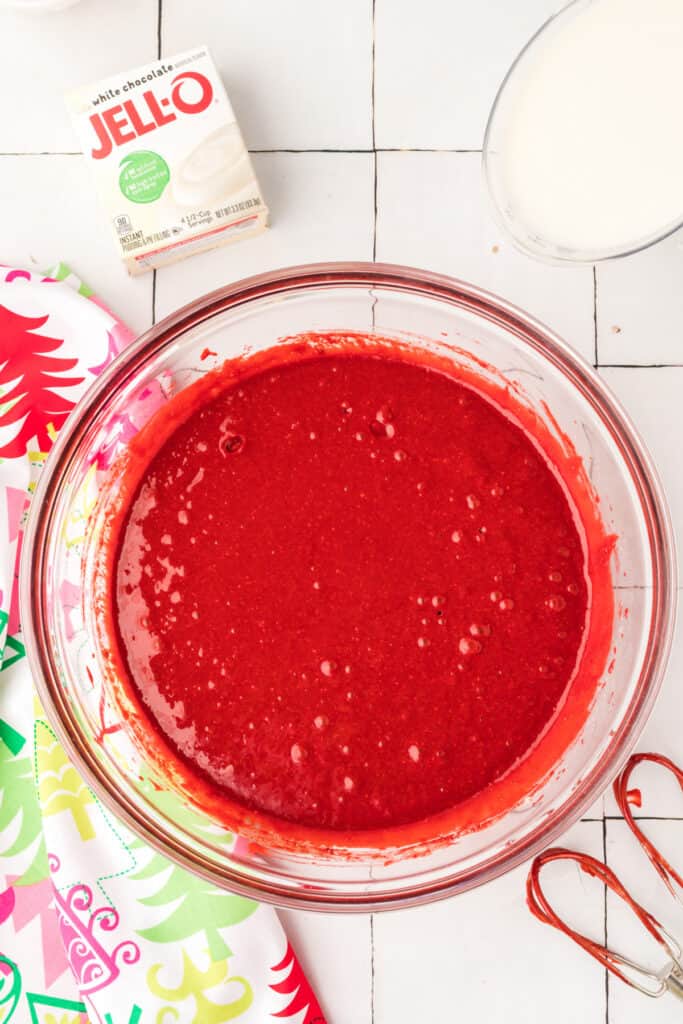Overhead view of red velvet cake batter fully mixed in a glass bowl with a whisk beside it.