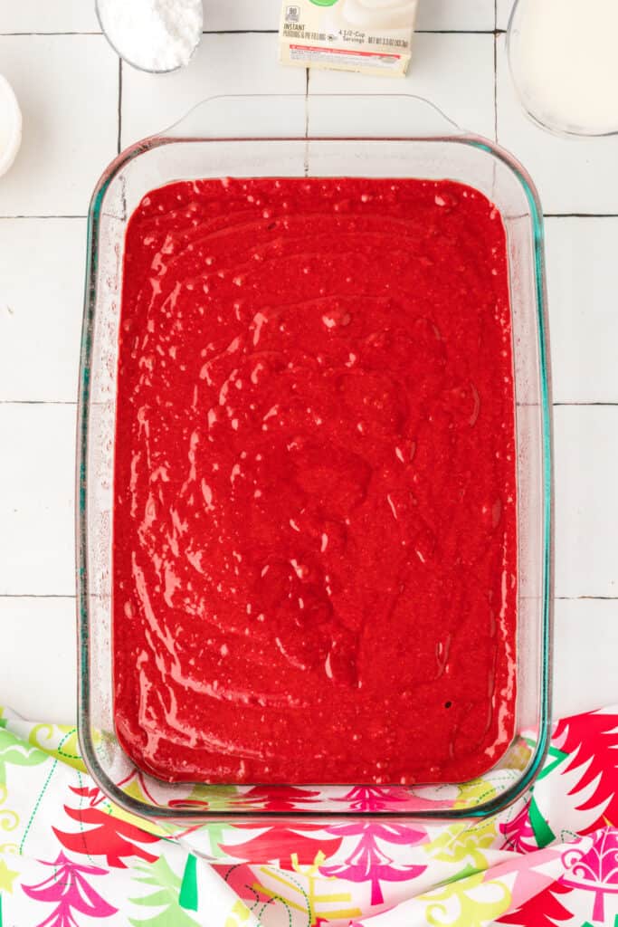 Red velvet cake batter spread evenly in a 9x13-inch glass baking dish before baking.