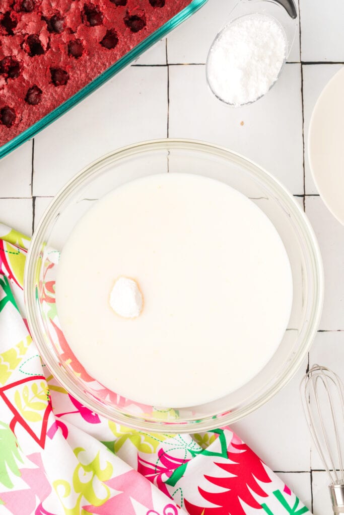 White chocolate instant pudding mix being combined with milk in a glass mixing bowl.
