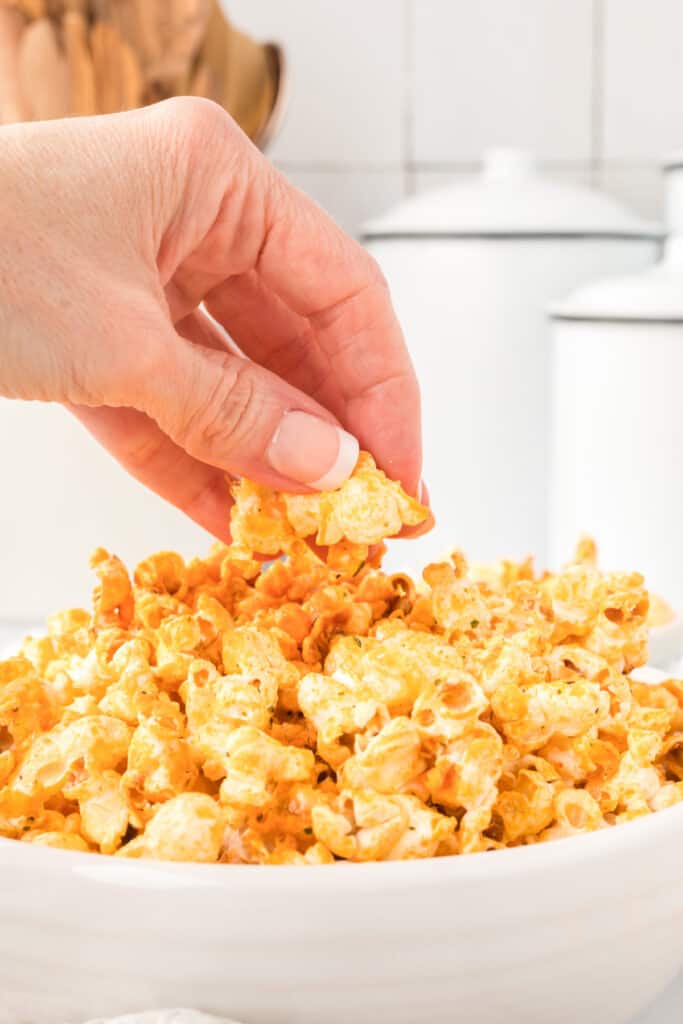 Hand grabbing Buffalo Ranch Popcorn from a bowl for an easy game-day snack
