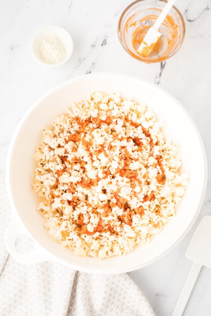 Buffalo sauce mixture drizzled over popcorn in a large bowl for Buffalo Ranch Popcorn