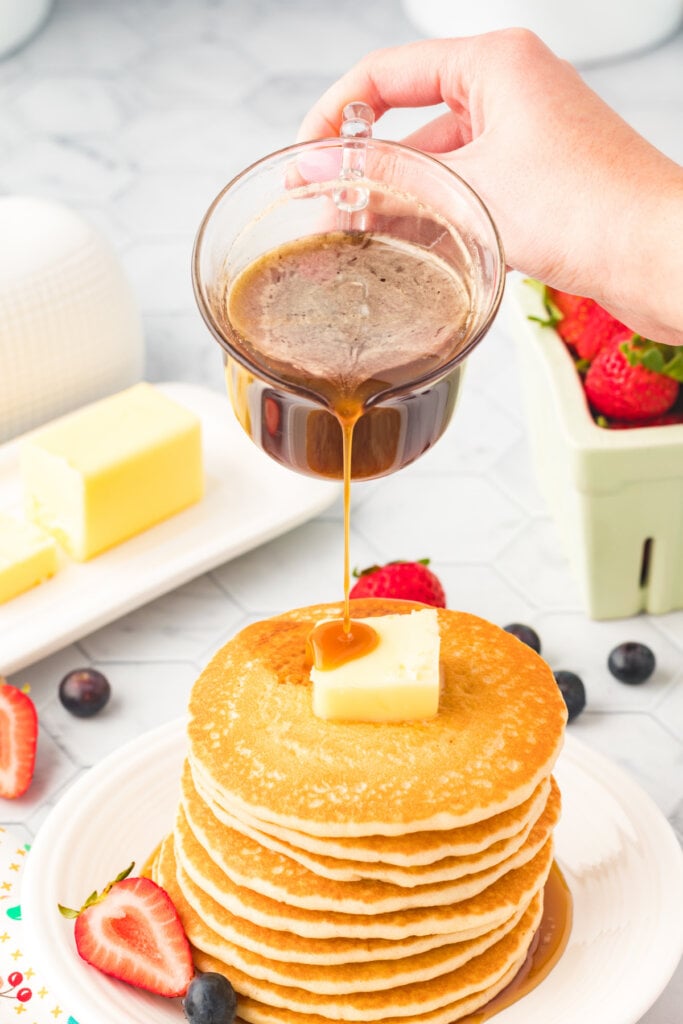 hand pouring pancake syrup over a stack of pancakes