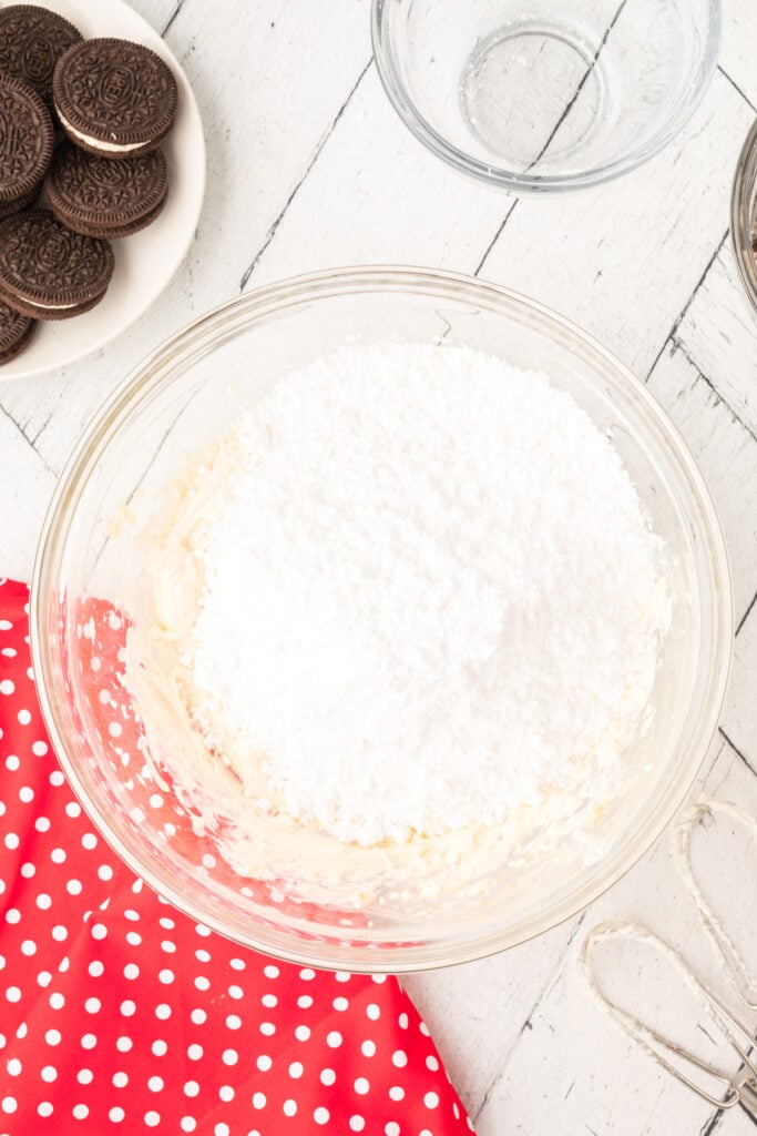 Glass mixing bowl with powdered sugar added on top of the creamed mixture before mixing.