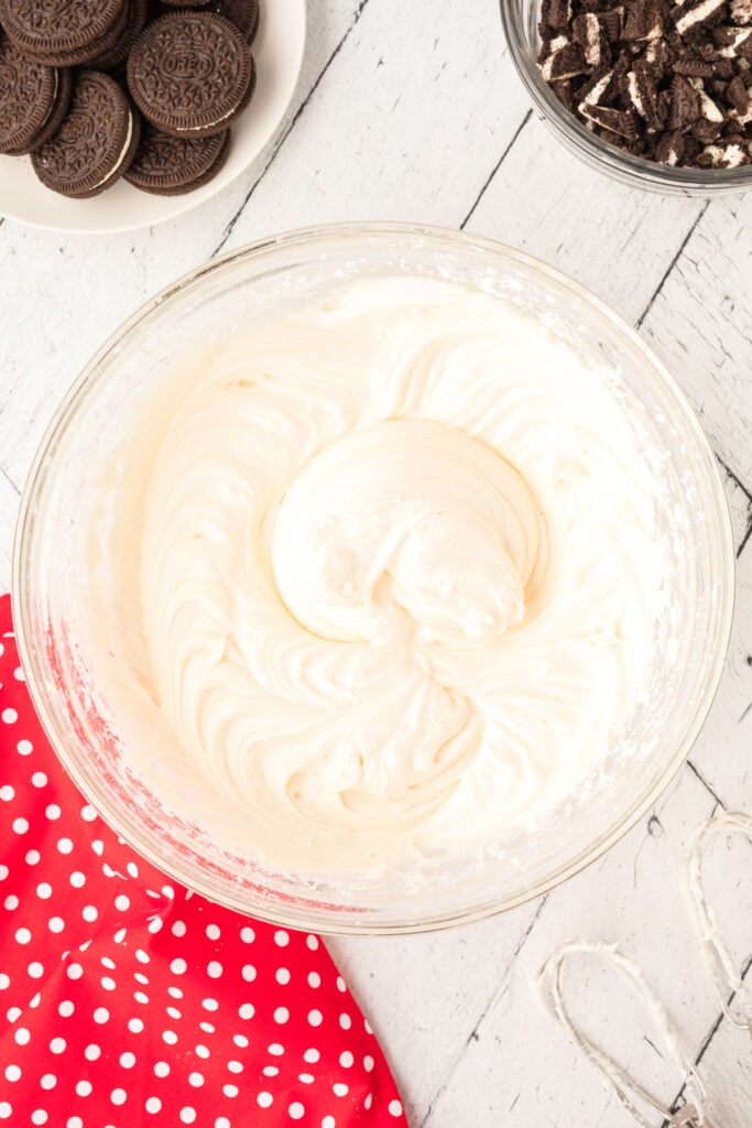 Glass mixing bowl with smooth, thick cream cheese frosting mixture and crushed Oreos in a separate bowl nearby.