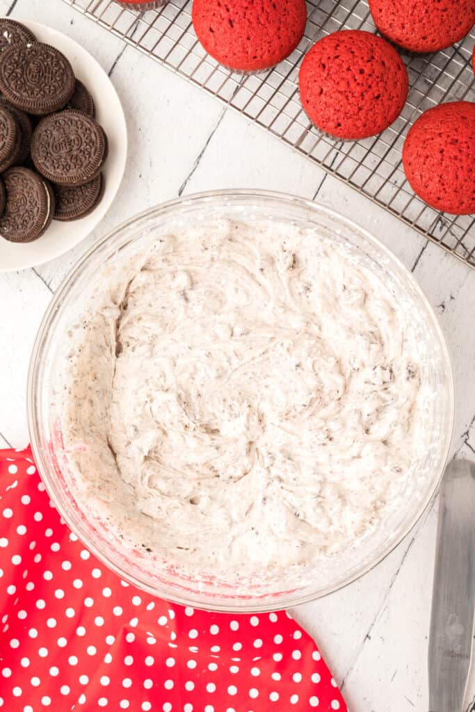 Glass mixing bowl with Oreo pieces folded into the cream cheese frosting, creating a speckled mixture.