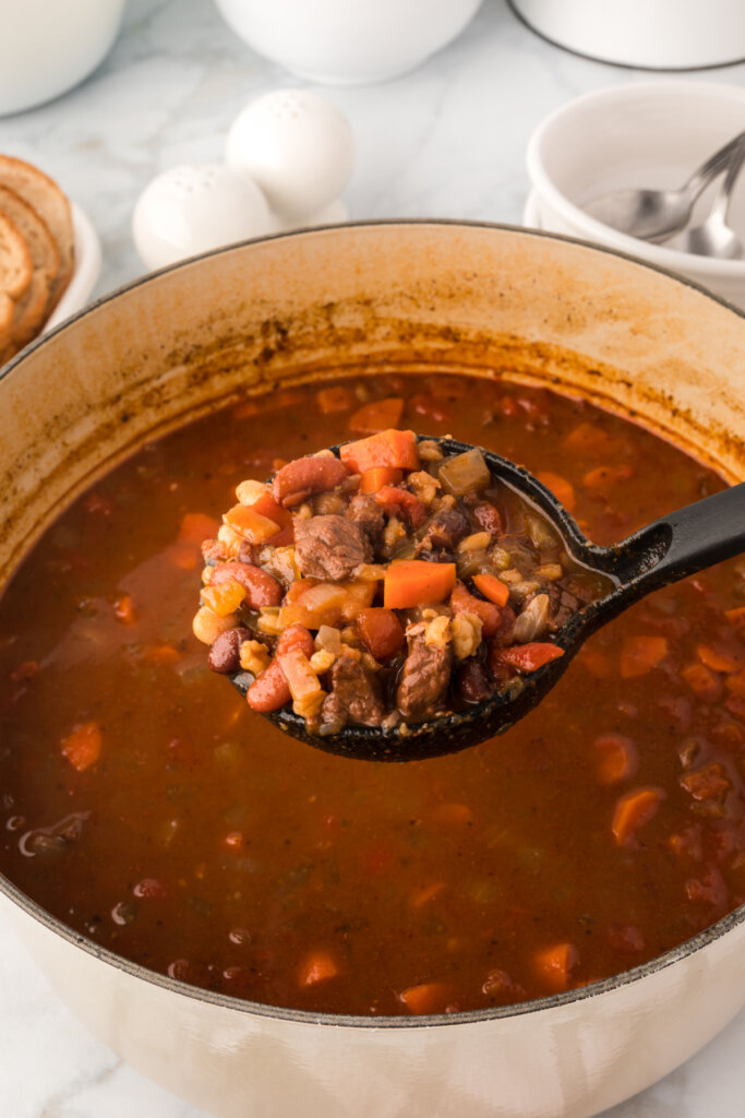 ladle of beef and barley soup over pot