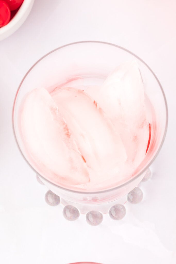 lear glass with ice and faint red tint from grenadine beginning to mix