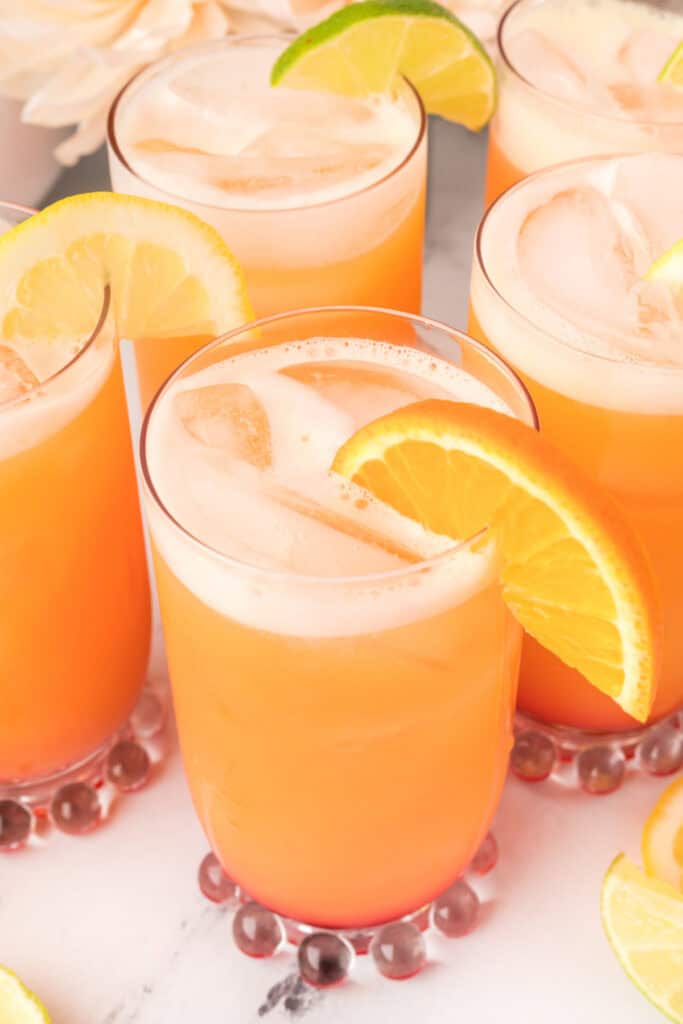 Close-up of Cactus Cooler recipe drinks with orange and lime garnishes, frothy tops, and tropical citrus colors