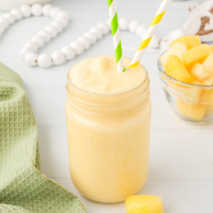 pineapple orange smoothie in mason jar with one green straw and one yellow straw