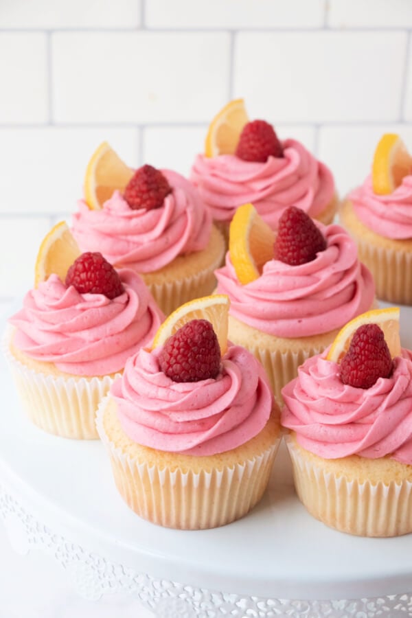 easy lemon cupcakes recipe with raspberry buttercream frosting on white cake stand