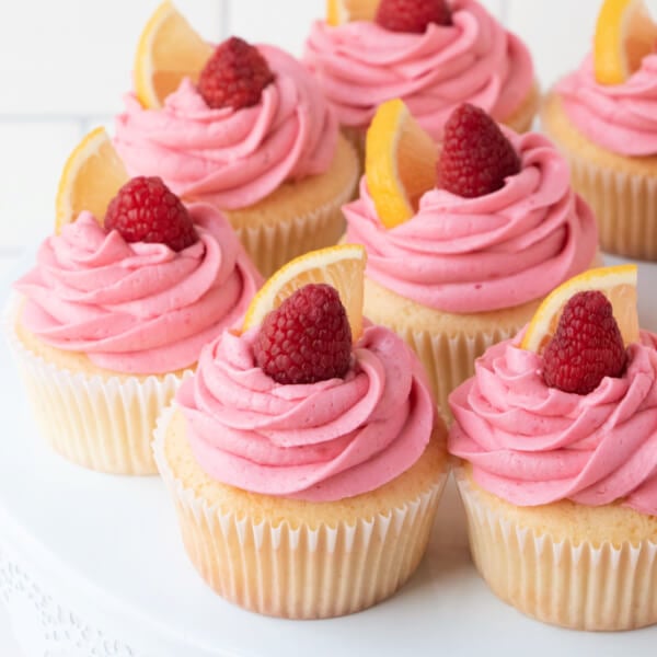 closeup of lemon cupcakes woth raspberry buttercream frosting on white cake stand