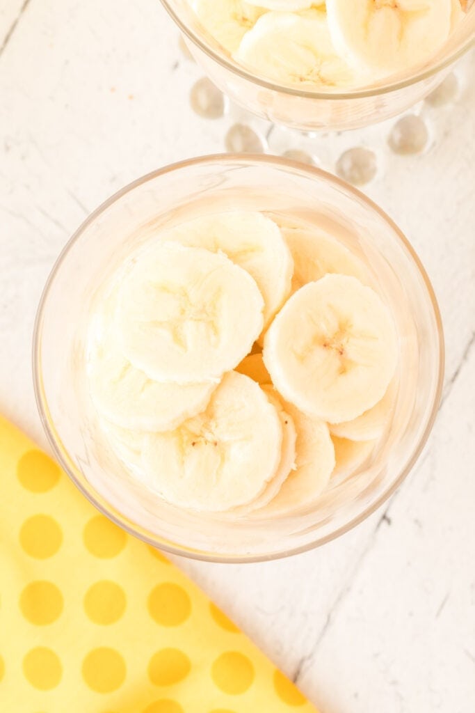 sliced bananas layered in a glass dessert cup for banana pudding parfait