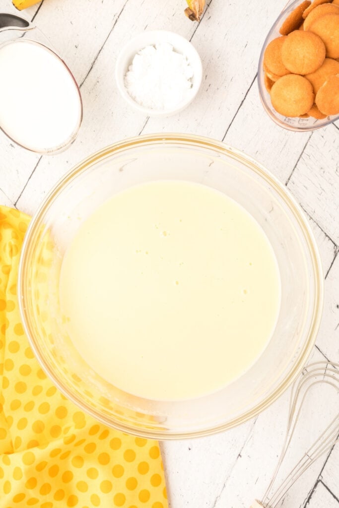 banana pudding mixture whisked smooth in a glass bowl with whisk and ingredients around