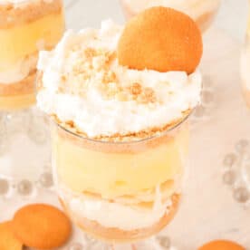 square image of banana pudding parfait in a glass cup with layered pudding, bananas, whipped cream, and cookies