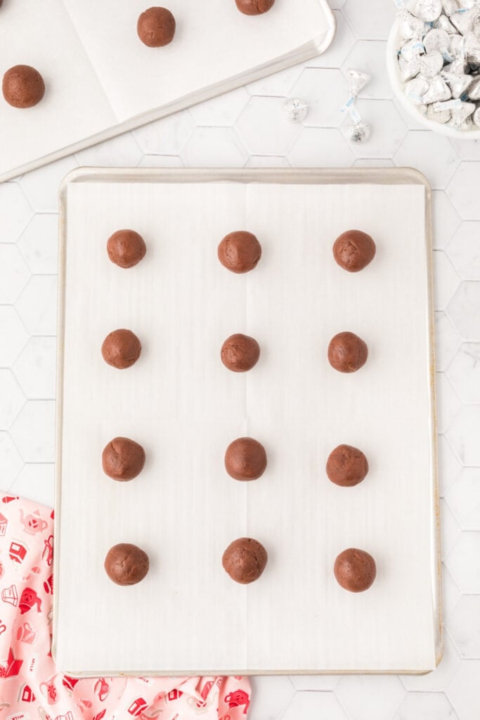 Rolled Chocolate Blossoms cookie dough balls arranged on parchment-lined baking sheets before baking