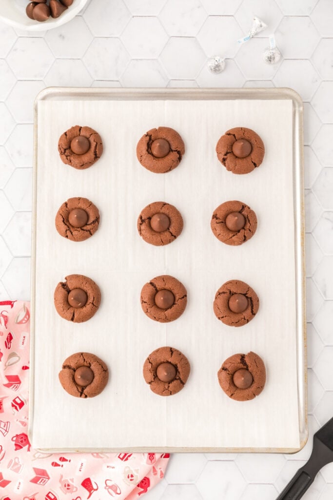 Freshly baked Chocolate Blossoms topped with milk chocolate Hershey's Kisses on a baking sheet