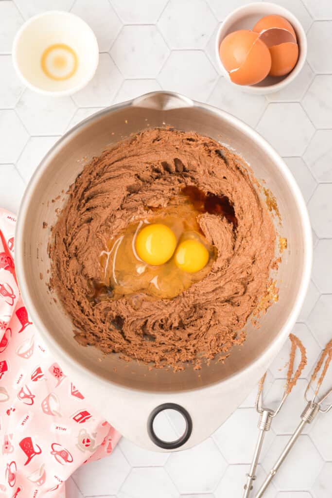 Eggs and vanilla extract added to creamed chocolate cookie mixture in a mixing bowl