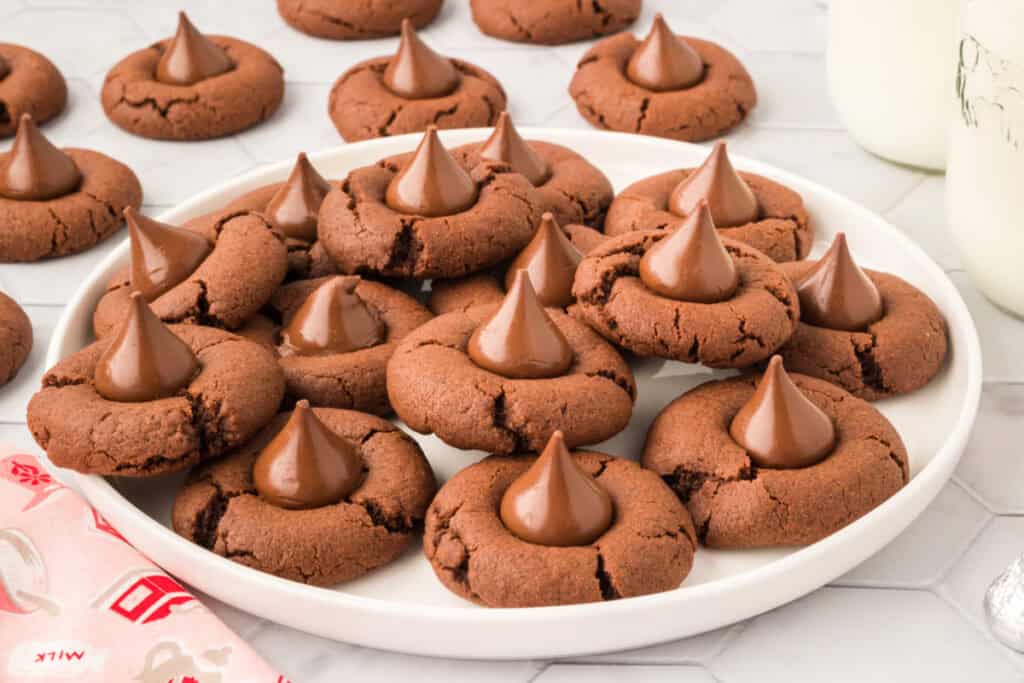 Plate of Chocolate Blossoms cookies topped with Hershey's Kisses surrounded by additional cookies and bottles of milk