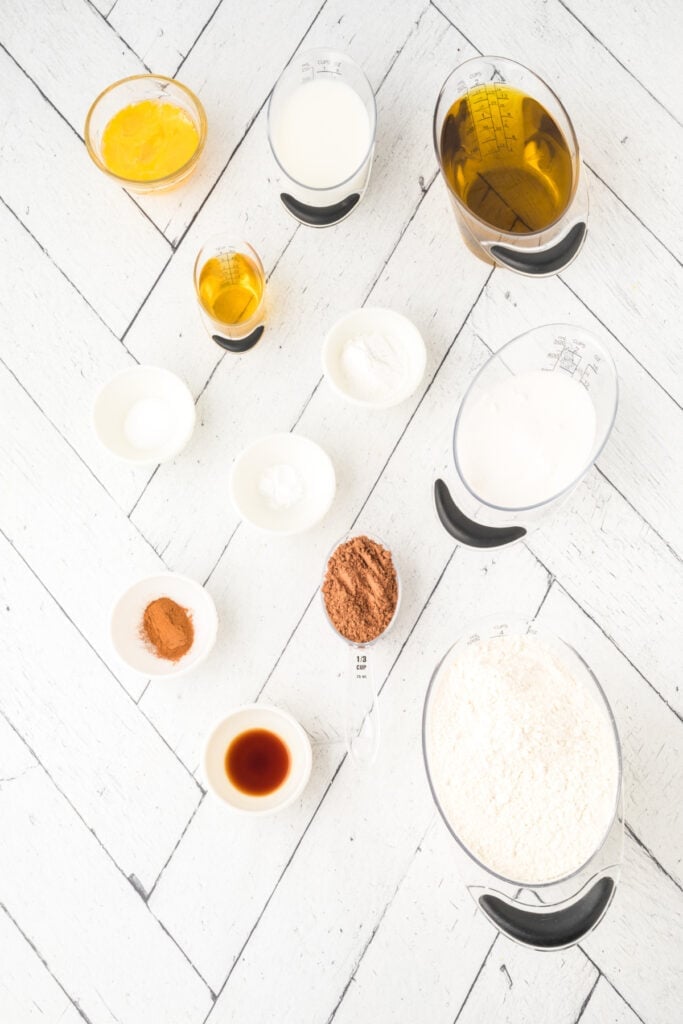 Overhead view of measured ingredients for chocolate cinnamon doughnuts on a white herringbone surface.