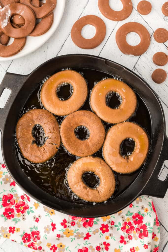 Chocolate doughnuts frying in hot oil in a black cast iron skillet.
