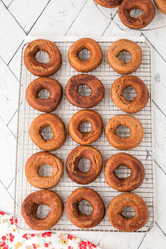Freshly fried doughnuts cooling on a wire rack over a floral cloth.