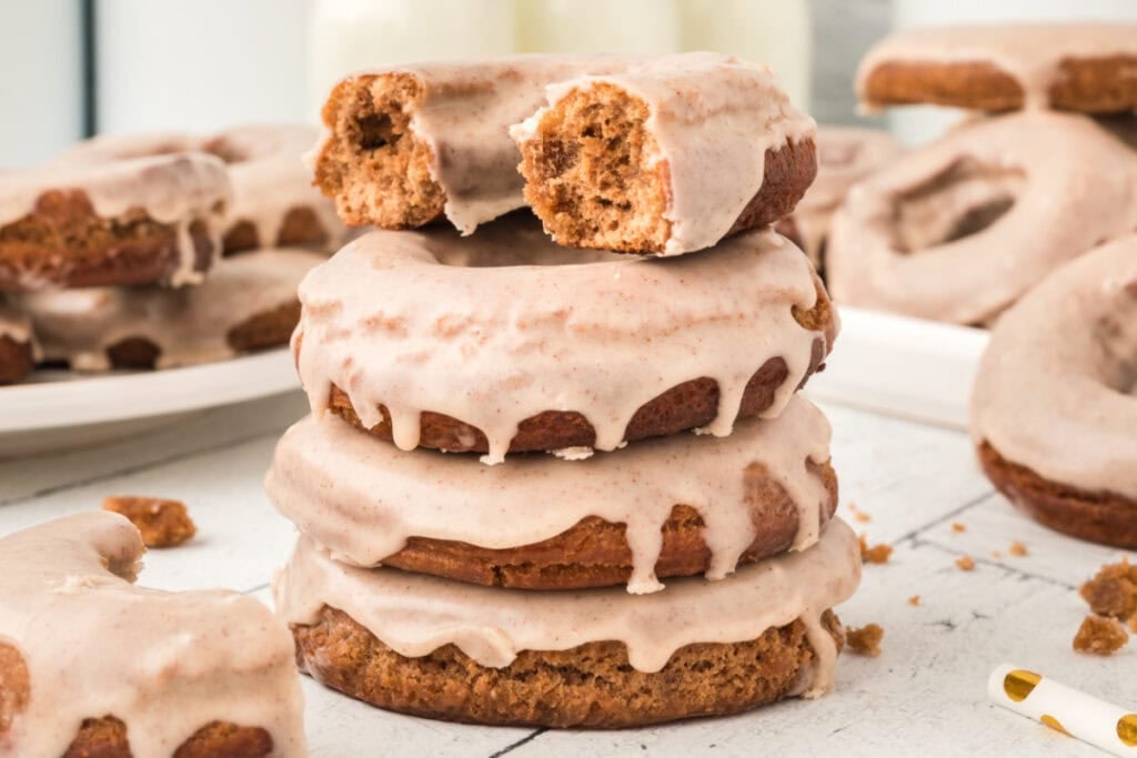 Wide shot of a stack of glazed doughnuts with one bitten doughnut on top, surrounded by more doughnuts.