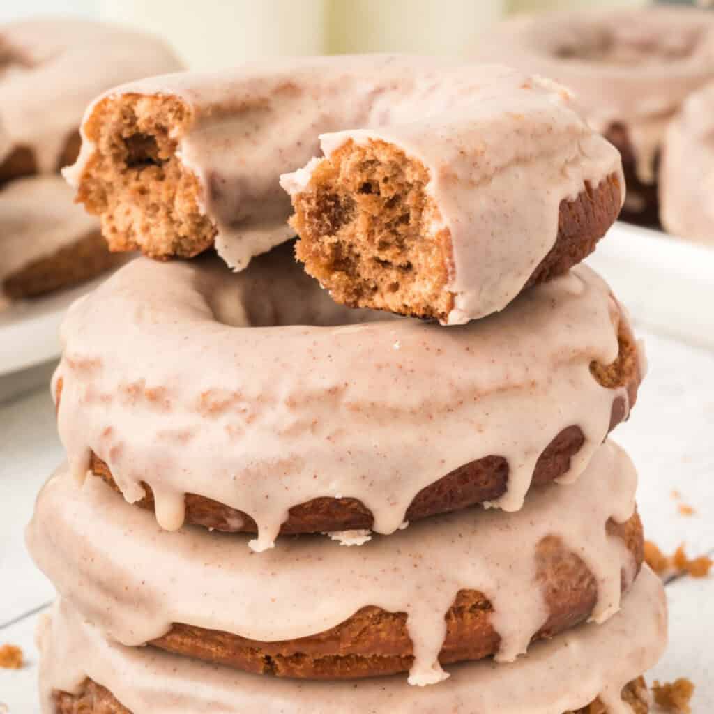 Square crop of a bitten chocolate cinnamon doughnut stacked on others, showing the texture inside.