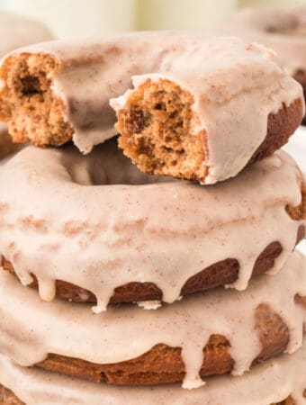 Square crop of a bitten chocolate cinnamon doughnut stacked on others, showing the texture inside.