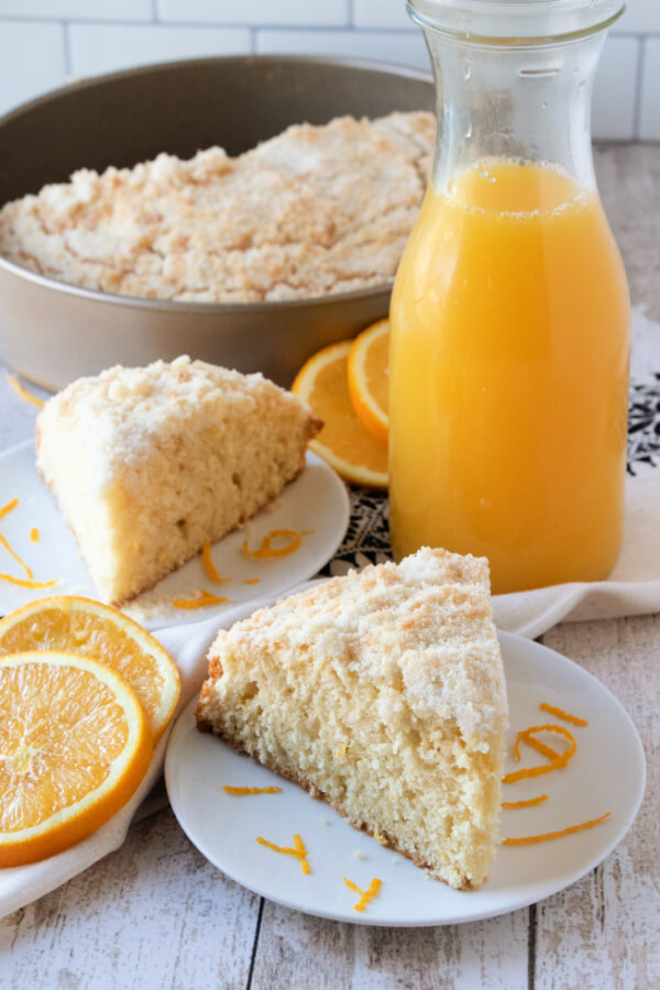 slice of coffee cake on plate with pitcher of orange juice in background