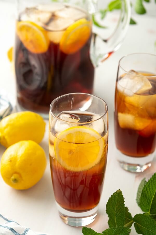 two glasses of tea with lemon and a pitcher of tea in background