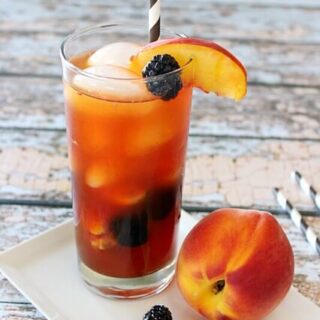 Jose Cuervo Iced Teagarita consists of the classic limeA Peach and Blackberry Teagarita in a glass with a peach next to the glass.