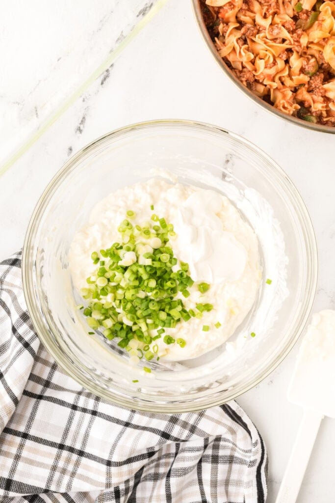 cottage cheese mixture with sour cream and chopped green onions in a glass bowl before mixing