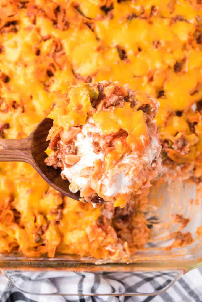spoon lifting a serving of beefy sour cream noodle bake showing layers of meat, noodles, and creamy filling