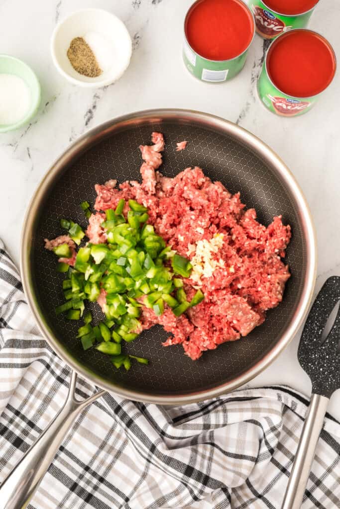 raw ground beef with chopped green pepper and minced garlic in a skillet before cooking