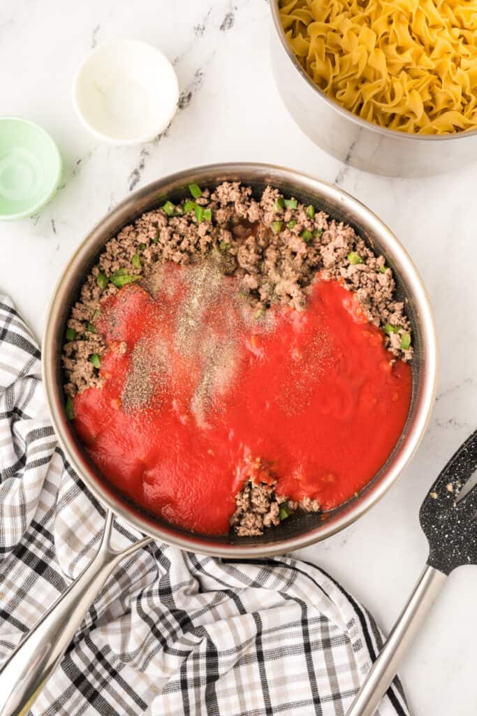 ground beef mixture in skillet with tomato sauce and seasonings added on top