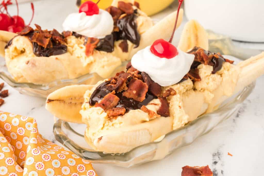 Close-up of an Elvis Banana Split topped with homemade peanut butter ice cream, hot fudge sauce, crispy bacon, whipped cream, and a maraschino cherry.