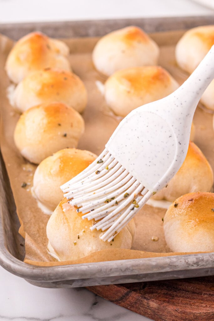 garlic and herb butter being brushed over the top of a cheese bomb