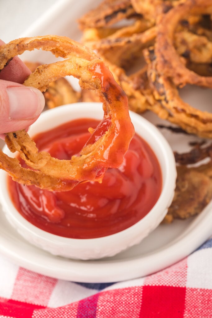 hand dipping two onion rings into ketchup