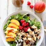 Peach & Raspberry Chicken Salad with Peach Vinaigrette in a bowl with fresh peaches and raspberries.