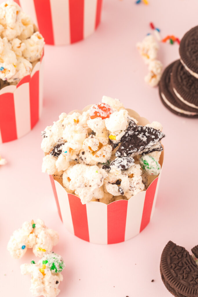 small red and white striped party cup filled with birthday cake popcorn mix