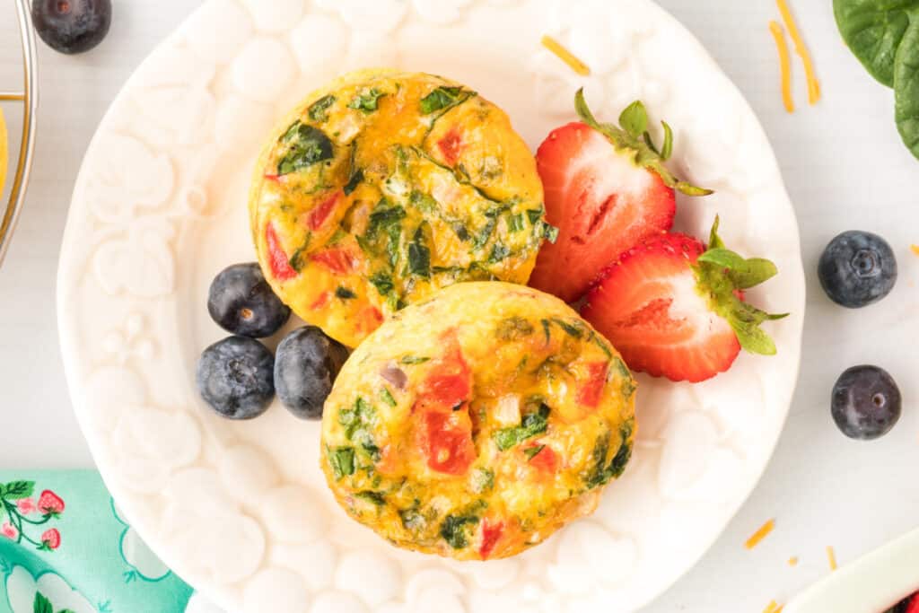 Two Breakfast Egg Muffins on a white plate with strawberries and blueberries